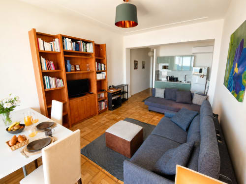 Modern apartment living room in Nice with blue sofa, wooden bookshelf, dining area and kitchen access