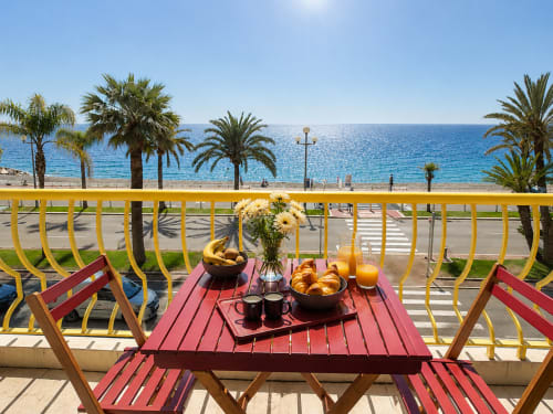 Sundeck apartment balcony in Nice with sea view, featuring breakfast setup overlooking beach and palm trees