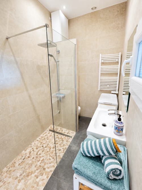 Modern bathroom in Sundeck apartment at Enjoy Nice hotel with walk-in shower, white sink, heated towel rack, and teal striped