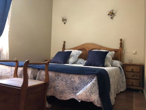 Acogedora habitación doble en Casa Rural El Infante de Oropesa con cama de madera, almohadas azul marino y decoración tradicional