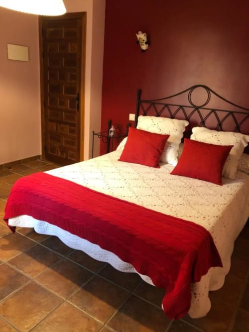 Elegante dormitorio doble en Casa Rural El Infante en Oropesa con detalles rojos, cama de hierro y piso de terracota