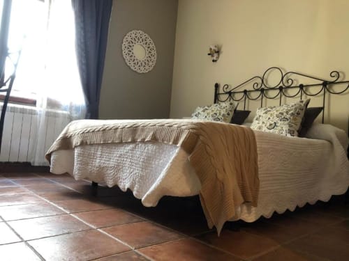 Espacioso dormitorio doble en Casa Rural El Infante con cama de hierro forjado ornamentado, ropa de cama crema y pisos de azulejo terracota