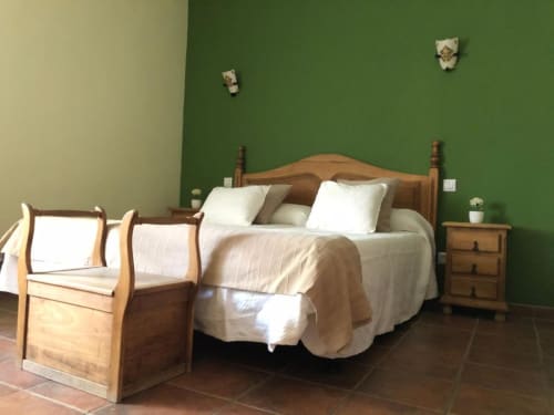 Cama rústica de madera con sábanas blancas y mesilla en dormitorio de paredes verdes en Casa Rural El Infante, Oropesa