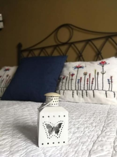 Linterna blanca decorativa con diseño de mariposa sobre cama con cojines florales en Casa Rural El Infante, Oropesa