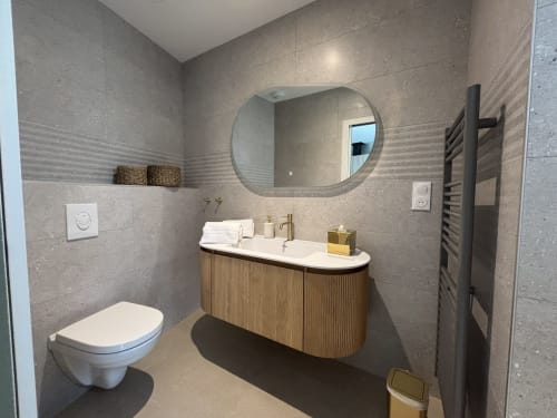 Salle de bain moderne à la Résidence Les 3 Volcans avec miroir rond, meuble vasque en bois et radiateur sèche-serviettes