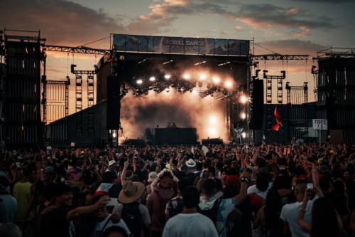 Escenario de festival musical al aire libre abarrotado con iluminación dramática y efectos de humo al atardecer cerca de Lyon
