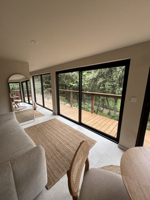 Élégant salon avec portes à cadre noir ouvrant sur une terrasse en bois dominant le jardin du Domaine d'Olga, Aniane