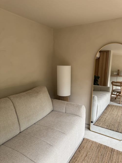 Chambre beige du Domaine d'Olga avec canapé crème, lampadaire cylindrique et miroir bombé reflétant la vue sur le jardin