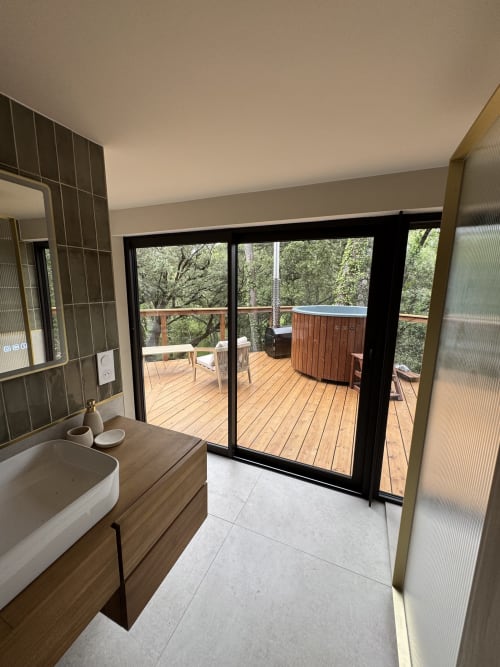 Salle de bain moderne avec vasque en bois donnant sur une terrasse en bois et le jardin du Domaine d'Olga, Aniane