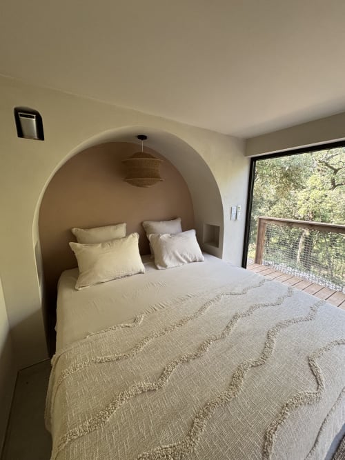 Chambre moderne avec lit en alcôve voûtée, literie crème, luminaire suspendu tressé et vue sur le jardin au Domaine d'Olga à Aniane