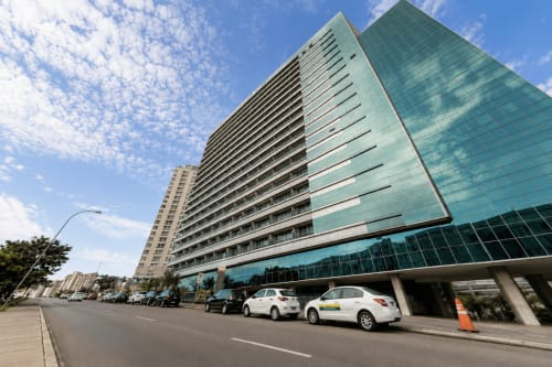 Moderno edifício hoteleiro de vários andares em Brasília com fachada de vidro, estacionamento no térreo e céu azul