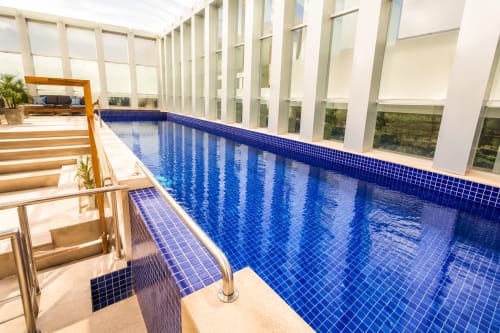 Piscina coberta com azulejos azuis no hotel ALUGUEASY em Brasília, com paredes de vidro modernas e área de descanso