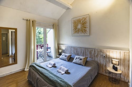 Chambre familiale lumineuse à l'Hôtel De La Bonnheure avec tête de lit en bois, accès au balcon avec vue jardin et mobilier moderne