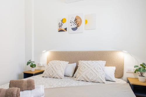 Dormitorio de cabaña junto al mar con cabecera beige, almohadas estampadas y arte botánico en Haus Holiday Homes