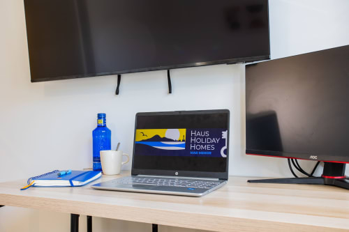 Espacio de trabajo moderno en Haus Holiday Homes con portátil, monitores duales, detalles azules y botella de agua sobre escritorio de madera