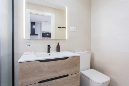 Baño moderno en De Lisa Duplex de Haus Holiday Homes, San Javier - espejo iluminado, tocador de madera, lavamanos blanco e inodoro