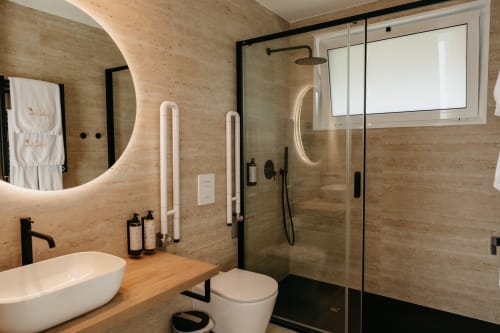 Banheiro moderno da Villa Diamante em Villas Eden com paredes de travertino, cuba de sobrepor, chuveiro tipo chuva e espelho com iluminação de fundo