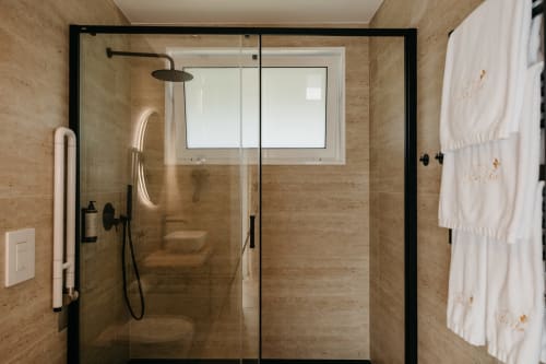 Banheiro moderno em Villas Eden com travertino, box de vidro e chuveiro tipo chuva na villa Vila Diamante