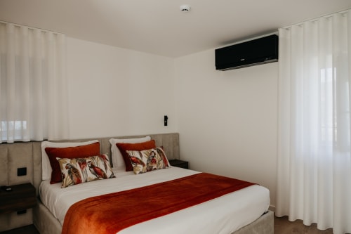 Quarto moderno da Vila Diamante com roupa de cama branca, detalhes em vermelho e ar-condicionado de parede
