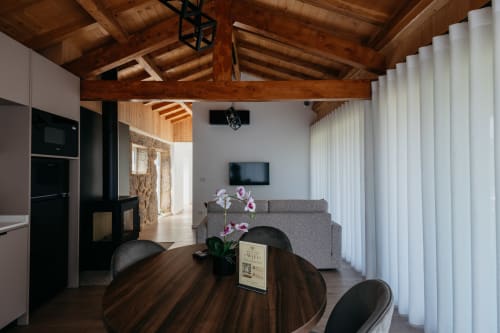 Interior moderno da vila em Villas Eden com vigas de madeira aparentes, mesa de jantar, sofá cinzento e cortinas brancas