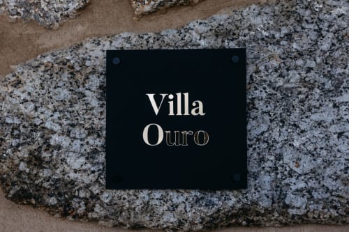 Placa de identificação preta com 'Villa Ouro' fixada em parede de pedra envelhecida na hospedagem boutique Villas Eden, Portugal