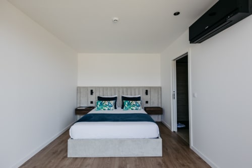 Quarto moderno na villa Villas Eden com cama queen, cabeceira estofada cinza, detalhes em azul-petróleo e piso de madeira