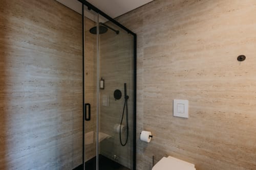 Banheiro moderno em Villas Eden com revestimento em travertino, chuveiro aberto, metais pretos e design contemporâneo