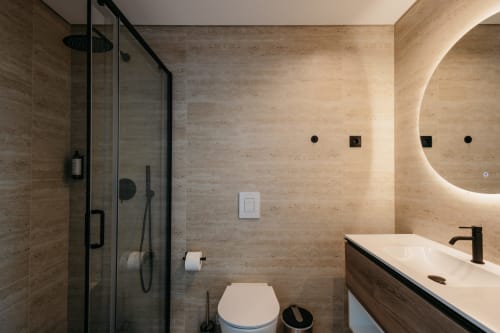 Banheiro moderno em Villas Eden com travertino, acabamentos pretos, espelho iluminado e chuveiro tipo walk-in