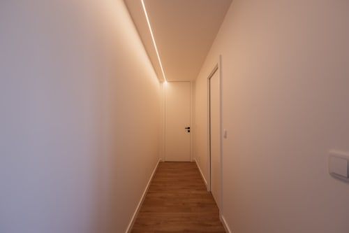 Corredor moderno da Villas Eden com iluminação LED aconchegante no teto, paredes brancas, piso de madeira e portas minimalistas