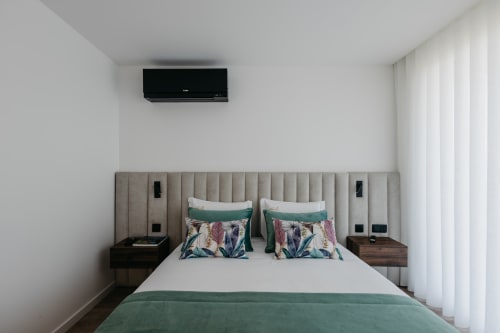 Quarto moderno em Villas Eden com cama queen, detalhes em azul-teal, ar-condicionado na parede e cortinas transparentes