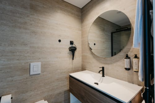 Banheiro moderno da villa Vila Onix em Villas Eden com ladrilhos de travertino, espelho redondo e torneiras pretas sofisticadas