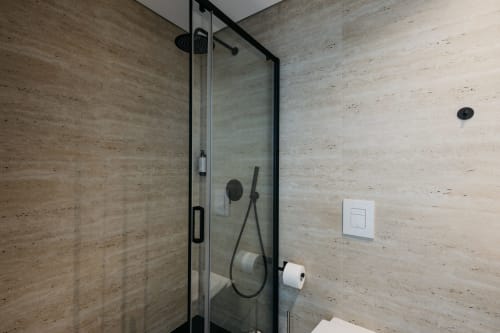 Chuveiro moderno com cabine envidraçada de moldura preta, revestimento em travertino e chuveiro tipo chuva na Vila Onix, Villas Eden