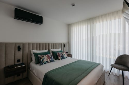 Quarto moderno na Villas Eden com cabeceira bege, roupa de cama verde e cortinas translúcidas com vista para Portugal