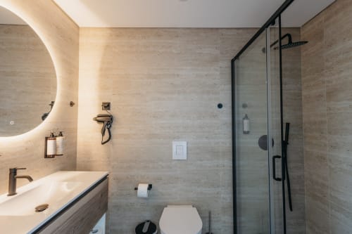 Banheiro moderno em Vila Quartz, Villas Eden com paredes de travertino, chuveiro tipo chuva, espelho iluminado e assento sanitário aquecido