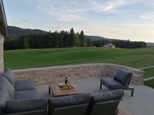 Terrasse extérieure du Gîte Les 3 Marches à Lamoura avec sièges, foyer et vue panoramique sur les montagnes