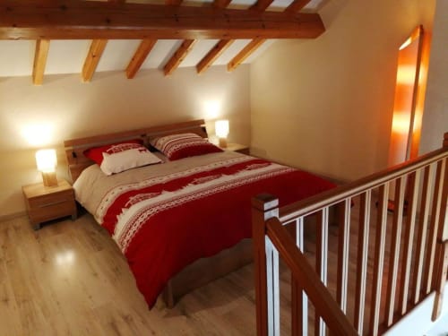 Chambre cosy du gîte Les 3 Marches à Lamoura : literie rouge, poutres bois et éclairage moderne