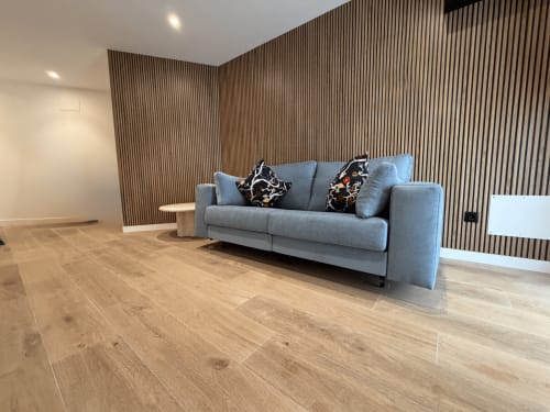 Moderna habitación de hotel en MTM Rooms con sofá gris, cojines decorativos, piso de madera y pared de acentos de listones verticales