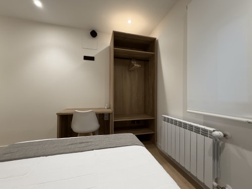 Habitación moderna de hotel MTM Rooms con cama, armario de madera, escritorio, silla blanca y radiador