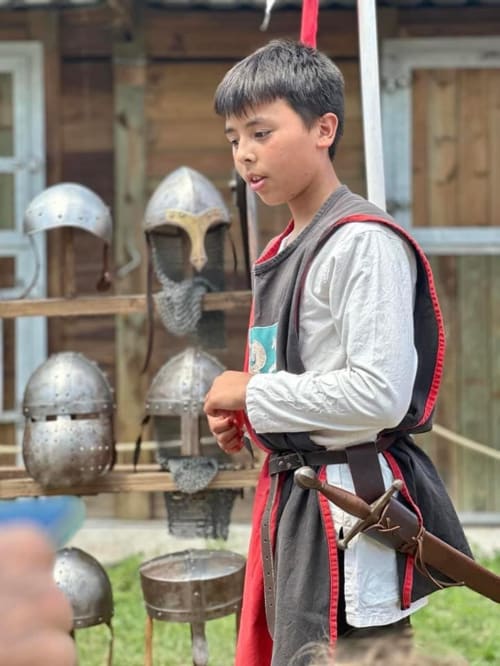 Jeune visiteur en costume d'armure médiévale à Châlus-Chabrol, explorant les expositions historiques et la présentation d'armes