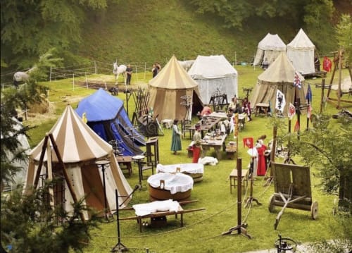 Campement de reconstitution médiévale au Domaine de Châlus-Chabrol avec tentes d'époque, drapeaux et visiteurs costumés à Châlus, France