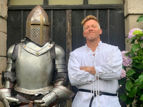Homme en tunique médiévale blanche posant avec chevalier en armure complète au Domaine de Châlus-Chabrol, Châlus France