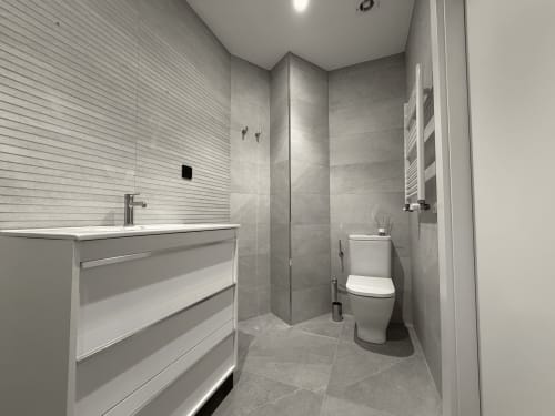 Baño moderno en el hotel MTM Rooms de Santander con azulejos grises, ducha a ras de suelo, lavamanos y inodoro