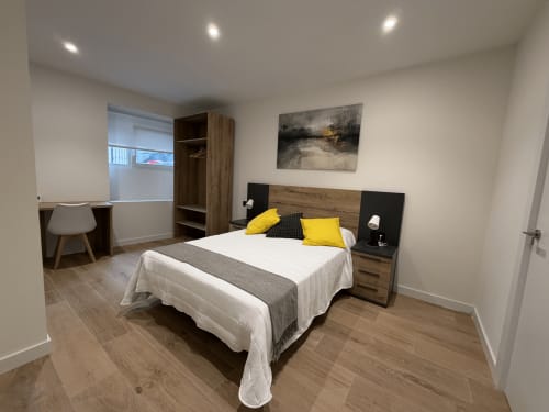 Moderna habitación doble en MTM Rooms Santander con cama de madera, detalles en amarillo y mobiliario contemporáneo