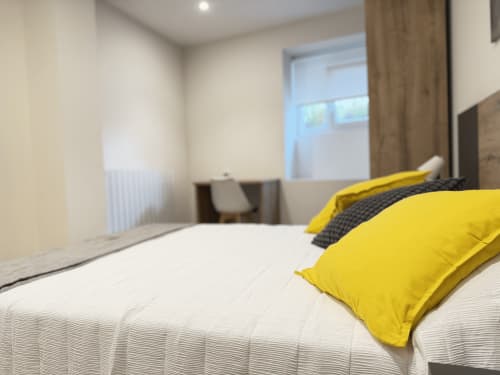 Moderno dormitorio doble en MTM Rooms de Santander con almohadas amarillas, ropa de cama blanca y luz natural abundante