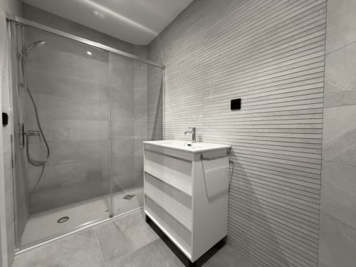 Baño moderno en MTM Rooms Santander con lavabo blanco, ducha de lluvia y paredes con azulejos horizontales