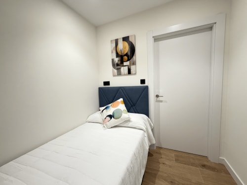 Dormitorio individual en MTM Rooms Santander con ropa de cama blanca, cabecero oscuro, suelo de madera y arte mural abstracto moderno