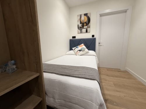 Habitación moderna en el hotel MTM Rooms de Santander con cabecero azul marino, ropa de cama blanca, suelo de madera y decoración contemporánea