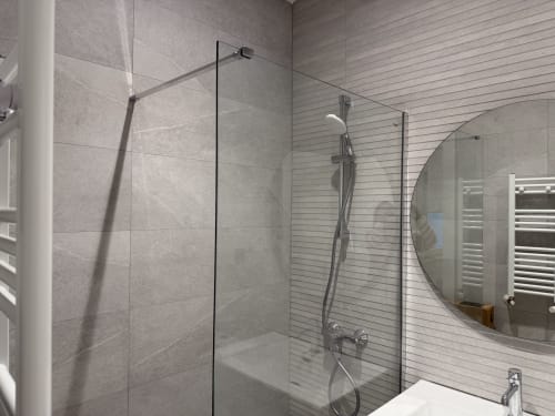 Baño moderno en MTM Rooms Santander con cabina de ducha de cristal, alcachofa de lluvia y espejo redondo