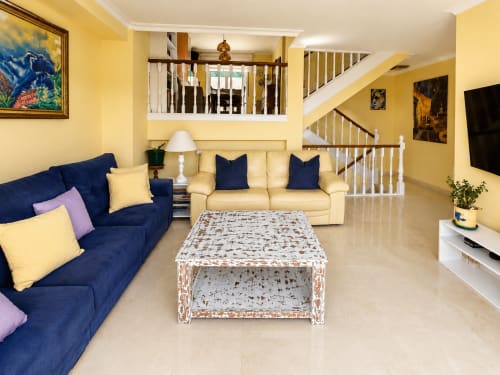 Luminosa sala de estar en amarillo brillante con sofás azul marino y crema, mesa de centro blanqueada y escaleras en la casa Alborada de Baiona
