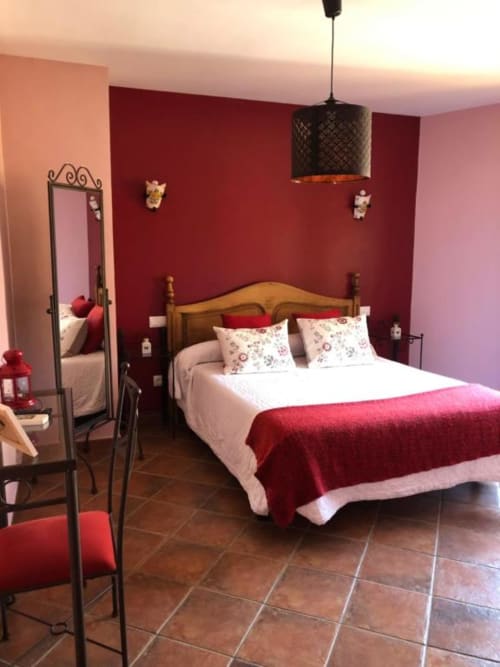 Elegante dormitorio doble en Casa Rural El Infante de Oropesa con paredes burdeos, cama de madera y lámpara colgante decorativa